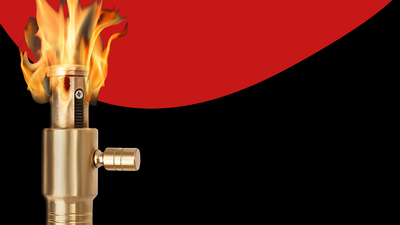 Close-up of a gold lighter emitting a powerful flame against a black and red background.