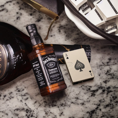 Ace of spades lighter and Jack Daniels whiskey bottle surrounded by luxury accessories, presented on a marble countertop.