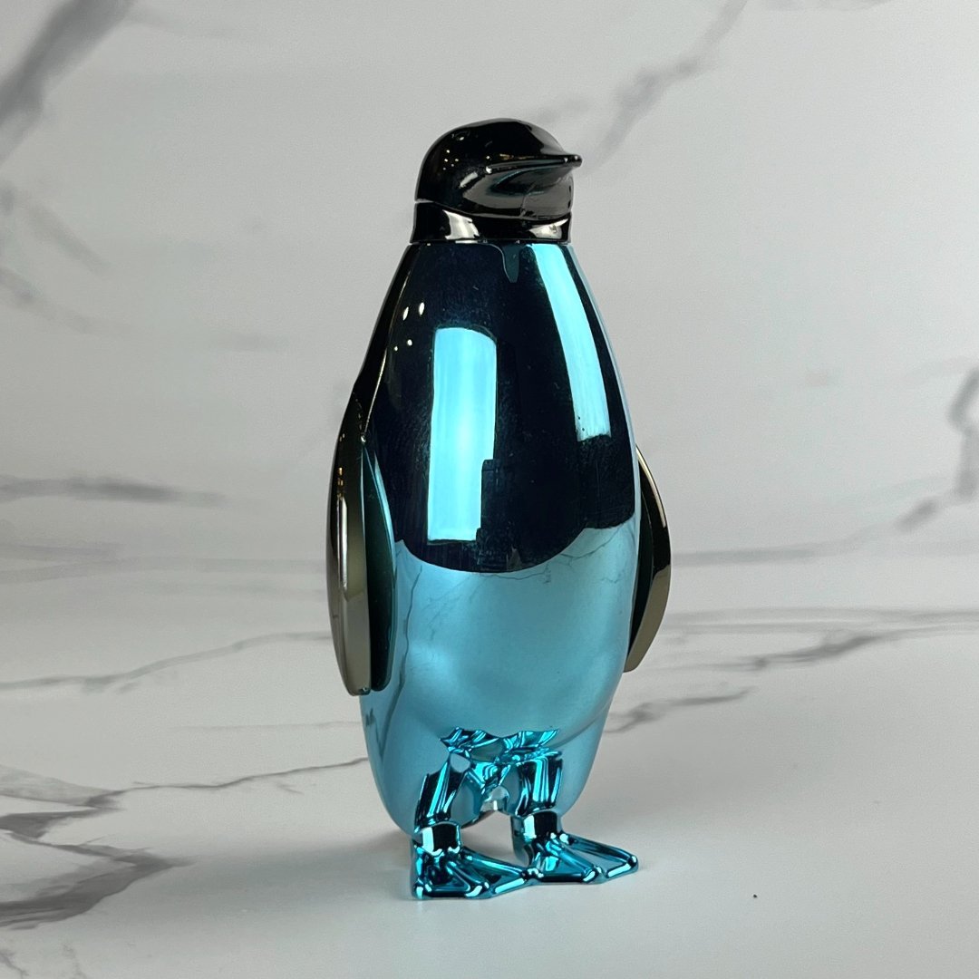 Sleek metallic blue penguin-shaped lighter with chrome wings and beak, standing upright on a marble backdrop.
