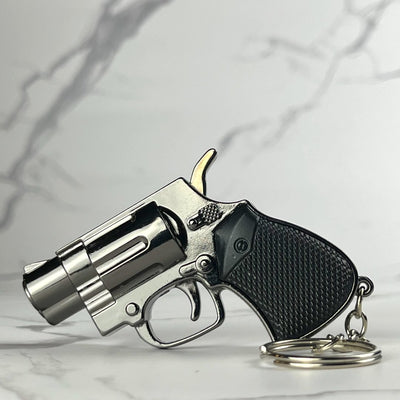 Miniature revolver-style torch lighter with black textured grip and chrome barrel, shown with keychain on marble surface.