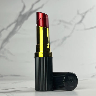 Black and gold lipstick-shaped refillable lighter featuring a red flame tip and ribbed cap design, displayed on marble surface.