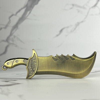 Brass-colored dagger-style refillable lighter featuring a curved fantasy blade and engraved guard, photographed on marble.
