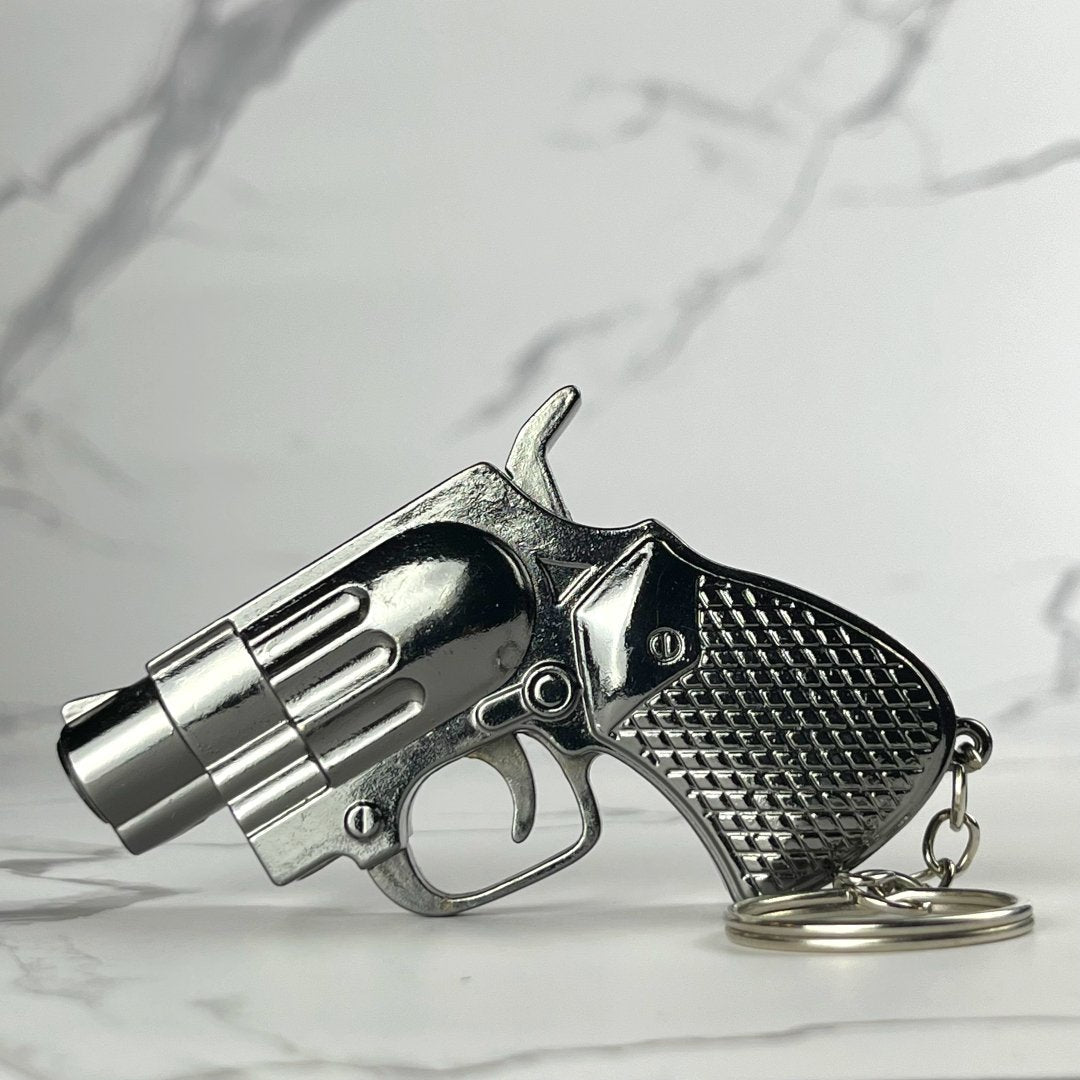 Miniature revolver-shaped refillable lighter with chrome grip and textured handle, includes keychain loop, displayed on marble background.