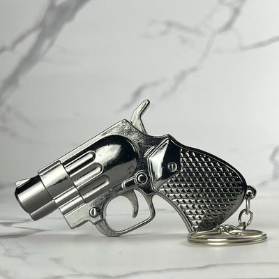 Miniature revolver-shaped refillable lighter with chrome grip and textured handle, includes keychain loop, displayed on marble background.