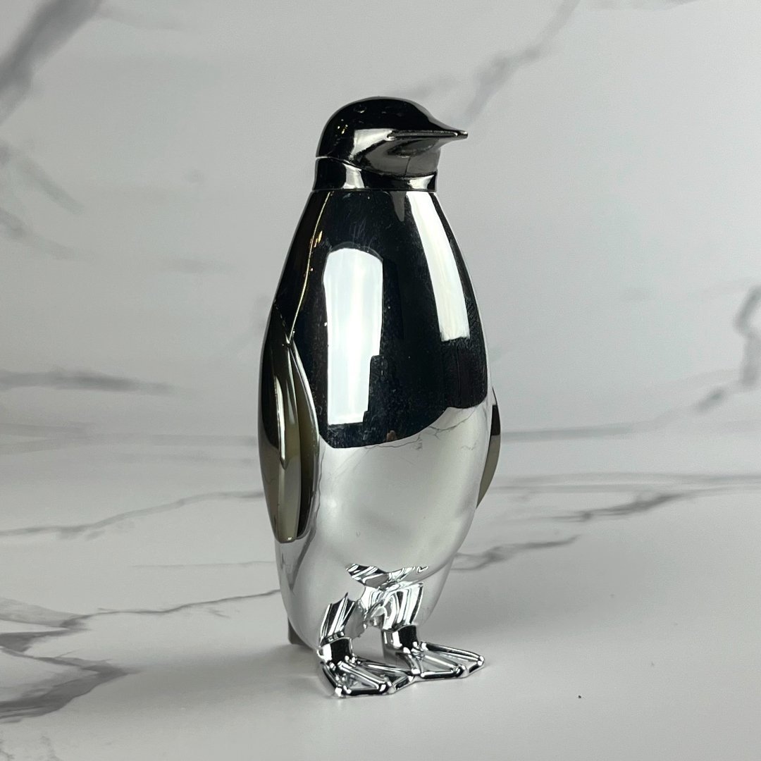 High-polish silver penguin lighter with reflective surface and minimalist design, posed on a white marble background.