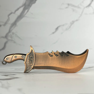 Ornate copper-colored dagger-shaped refillable lighter with engraved guard and curved blade, displayed on a marble surface.