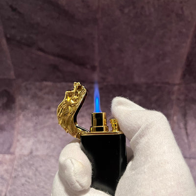 Black and gold dragon lighter with the dragon head flipped open, emitting a strong blue torch flame, held by a gloved hand.