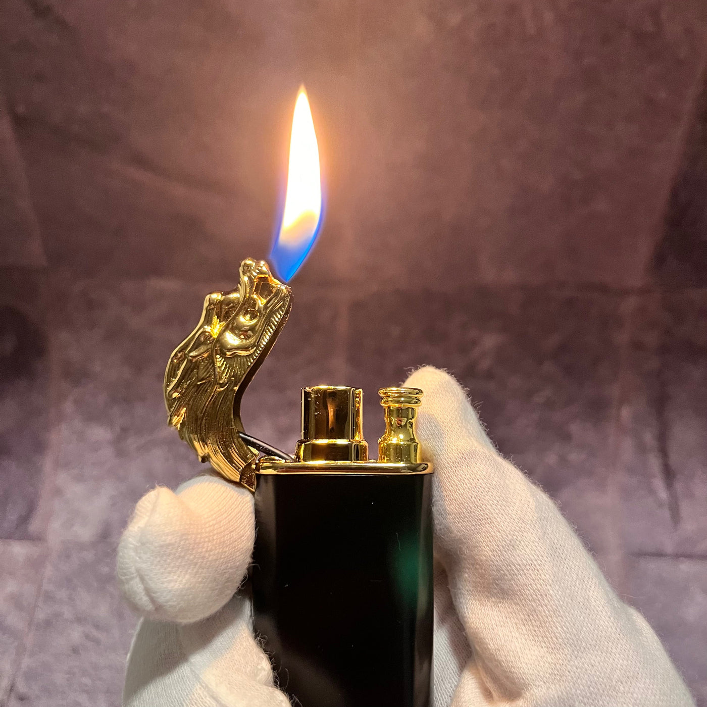 Black and gold dragon lighter producing a tall orange-blue flame, dragon head open, displayed in a gloved hand.