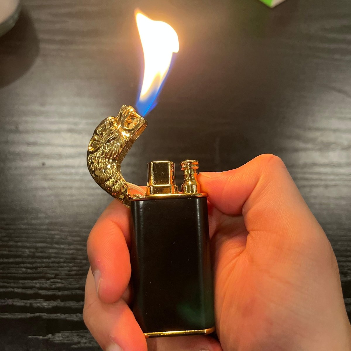Hand holding a black and gold dragon lighter with flame ignited.