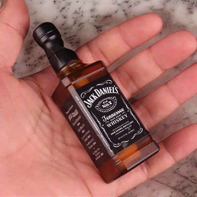 Miniature Jack Daniels whiskey bottle held in hand, highlighting its authentic design against a marble background.