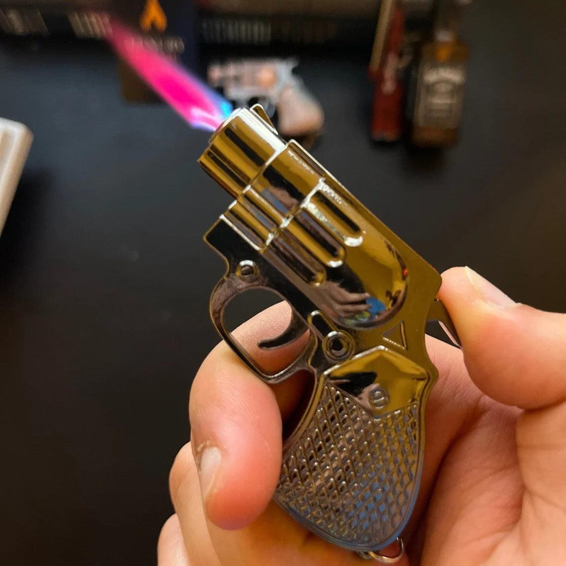 Miniature revolver lighter firing a blue torch flame while being held in hand, background blurred with product display.