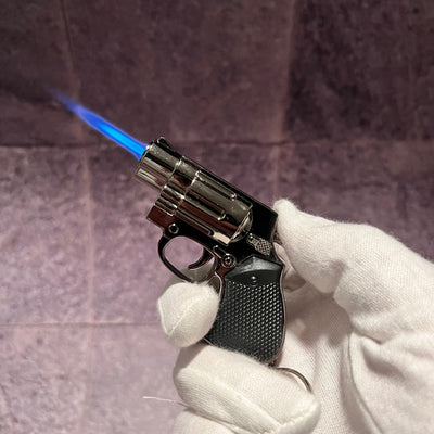 Miniature revolver refillable lighter with powerful blue flame, gripped in a white glove.