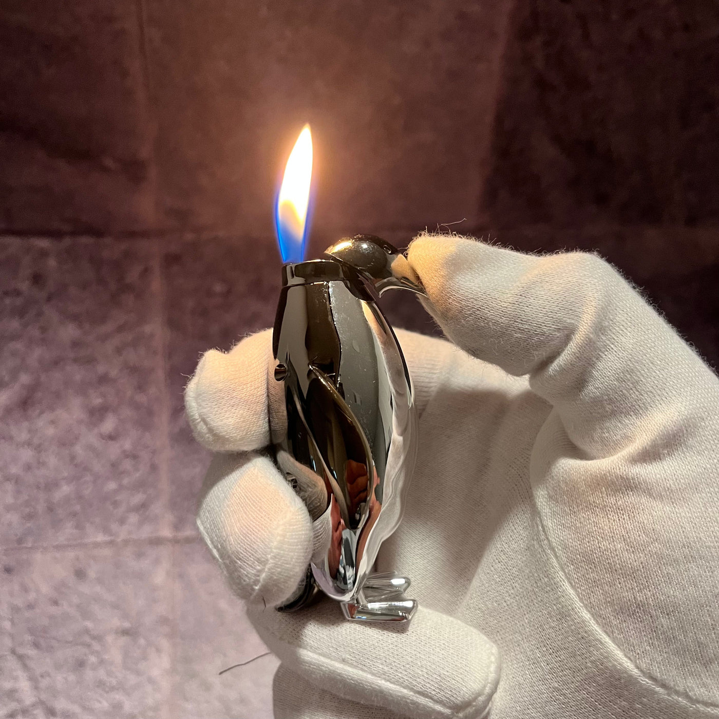 Penguin Flame Lighter – chrome silver refillable butane torch lighter shaped like a penguin, producing a powerful blue flame while held in a gloved hand.