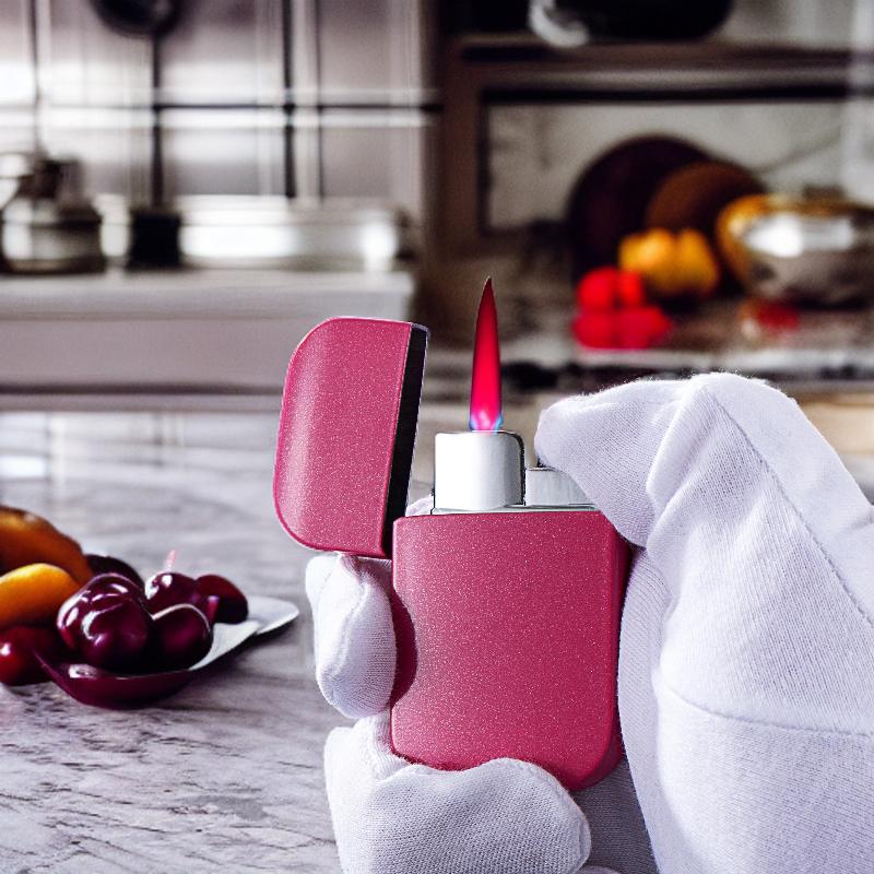 Pink torch lighter with a bright flame, held in a gloved hand, displayed on a kitchen countertop with fruit in the background.