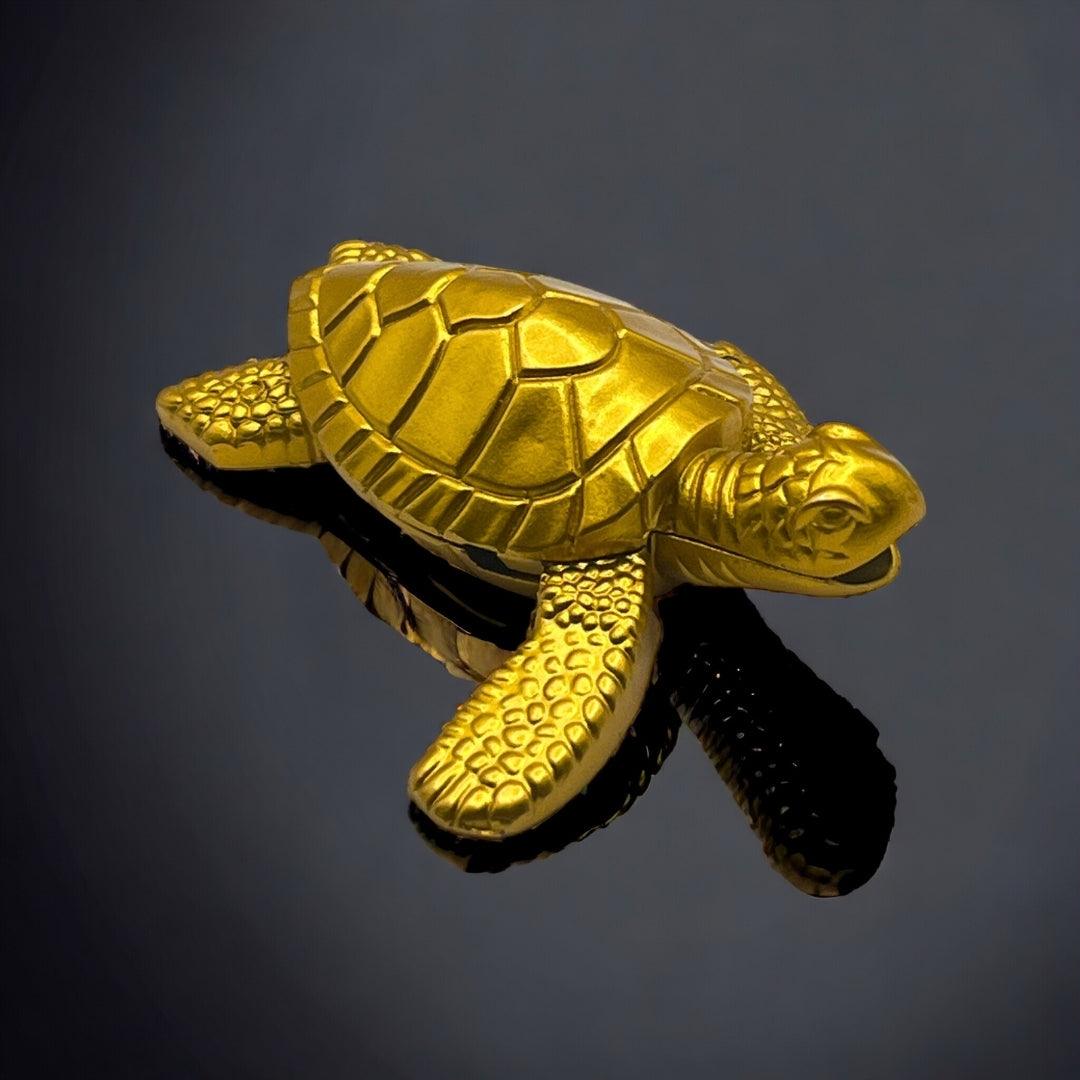 Sea Turtle Lighter – gold refillable butane lighter with detailed turtle shell design, displayed on glossy black reflective surface