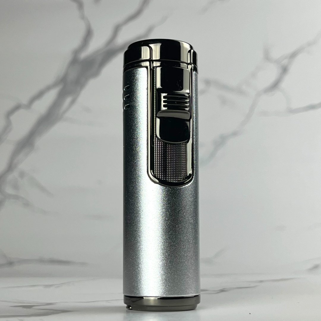 Modern silver torch lighter with glossy black ignition and side grip, standing vertically against a marble backdrop.