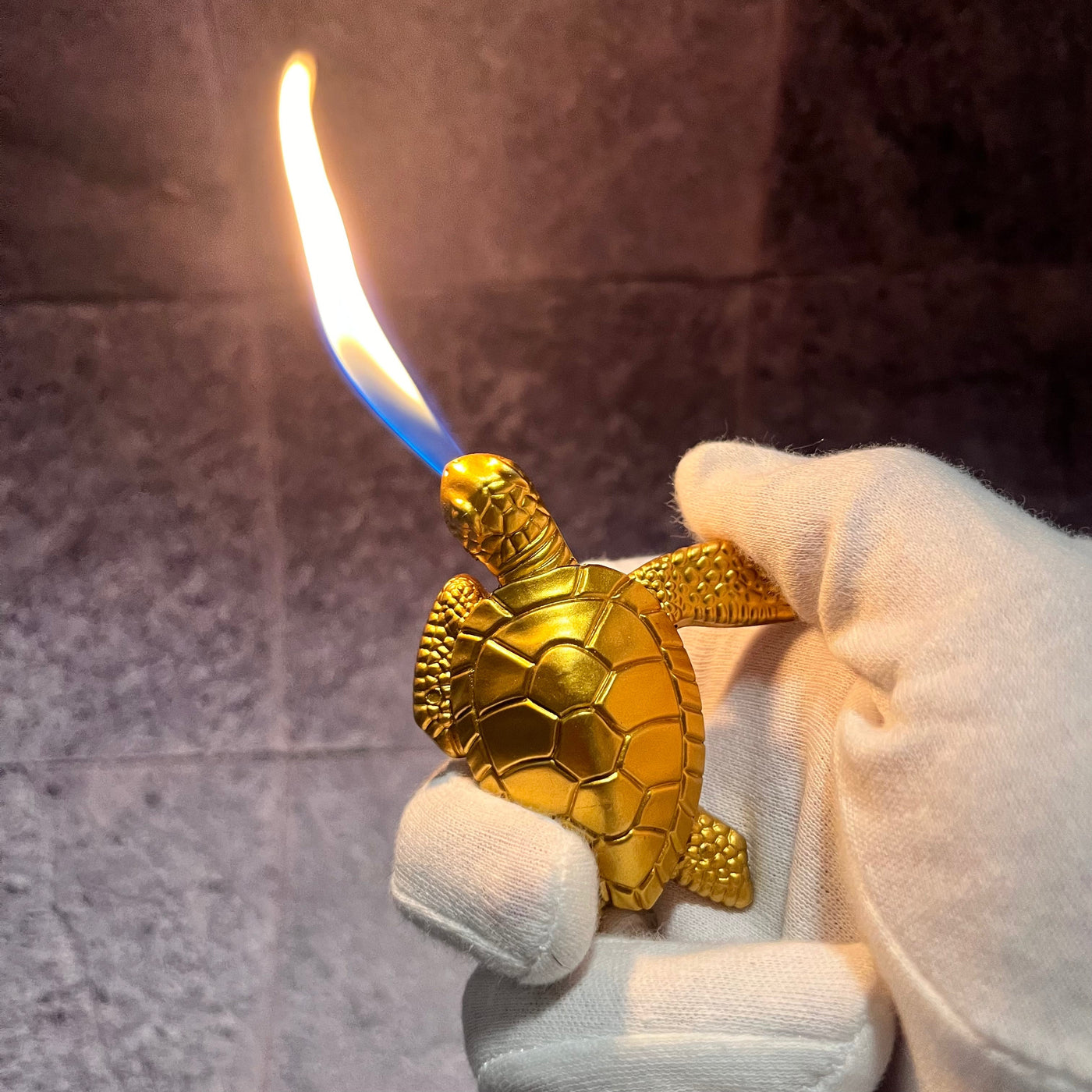Sea Turtle Lighter – gold refillable butane torch lighter shaped like a turtle, producing a bright blue flame while held securely in a gloved hand.