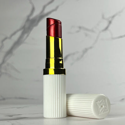 Realistic white and gold lipstick-style refillable lighter with a red flame tip, standing upright with cap beside it on marble background.